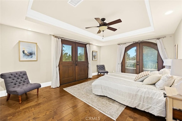 bedroom with dark hardwood / wood-style floors, ceiling fan, a raised ceiling, and french doors