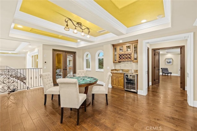 dining room with beverage cooler, dark wood-type flooring, a raised ceiling, bar area, and crown molding