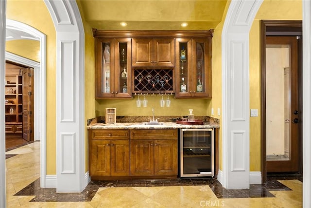 bar with wine cooler, light stone countertops, and sink