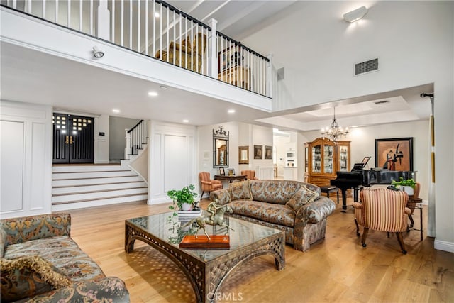 living room featuring a high ceiling, a chandelier, light wood-type flooring, and a tray ceiling