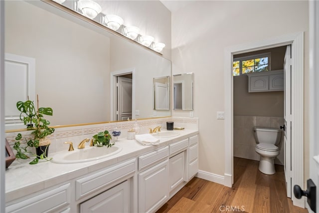 bathroom with vanity with extensive cabinet space, wood-type flooring, tile walls, dual sinks, and toilet