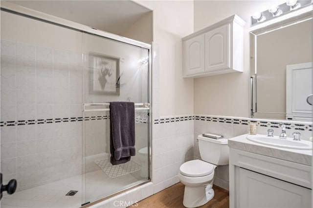 bathroom with tile walls, toilet, wood-type flooring, vanity, and a shower with door