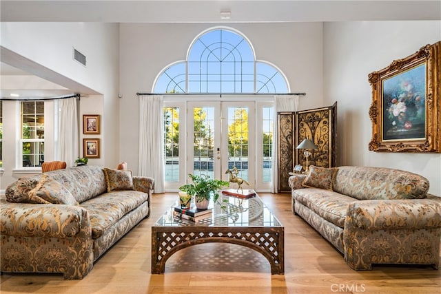 living room with french doors, light wood-type flooring, and a high ceiling