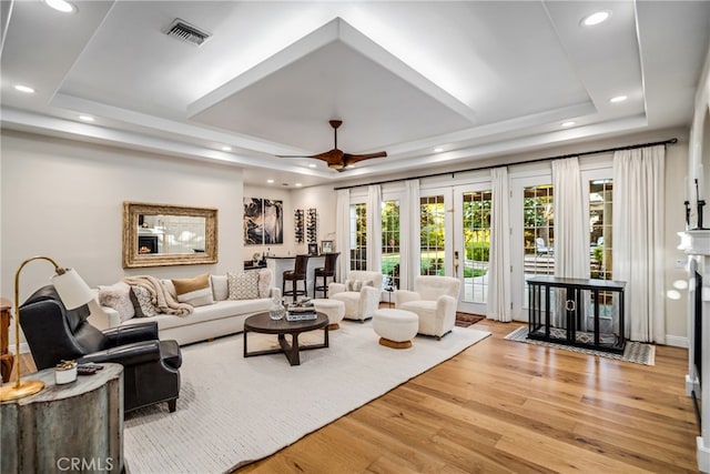 living room featuring french doors, light hardwood / wood-style floors, ceiling fan, and a raised ceiling