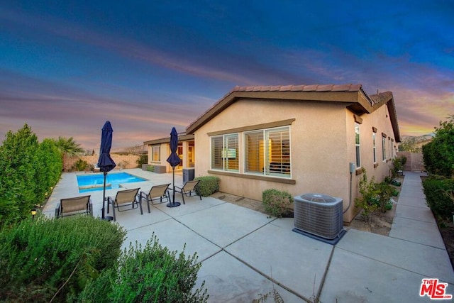 back house at dusk with a fenced in pool, a patio area, and central AC