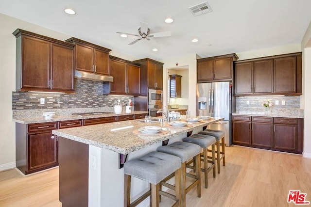 kitchen featuring tasteful backsplash, ceiling fan, light wood-type flooring, and an island with sink