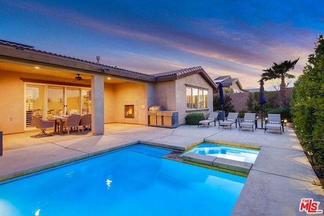 pool at dusk featuring a patio, grilling area, and an in ground hot tub