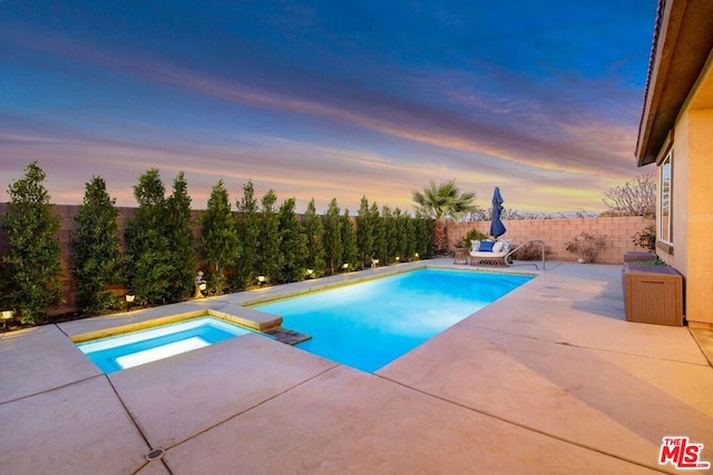 pool at dusk with a patio area and an in ground hot tub