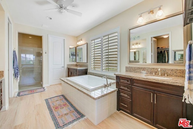 bathroom featuring ceiling fan, hardwood / wood-style floors, vanity, and a relaxing tiled bath