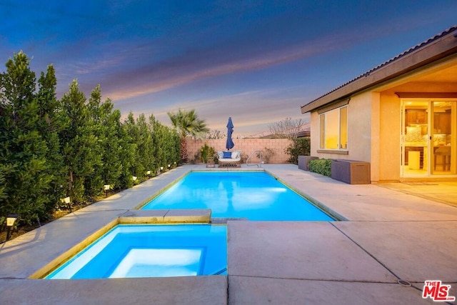 pool at dusk with an in ground hot tub and a patio