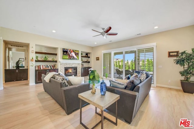 living room featuring built in features, ceiling fan, light wood-type flooring, and a fireplace