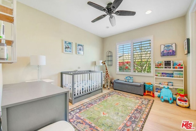 bedroom with ceiling fan, light wood-type flooring, and a nursery area