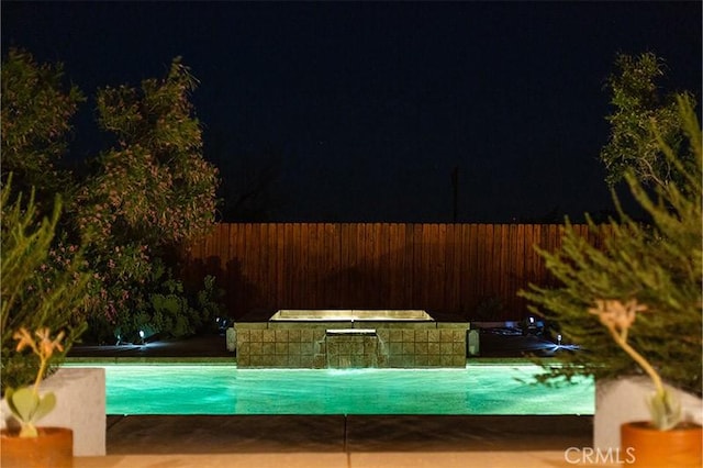 pool at night featuring pool water feature