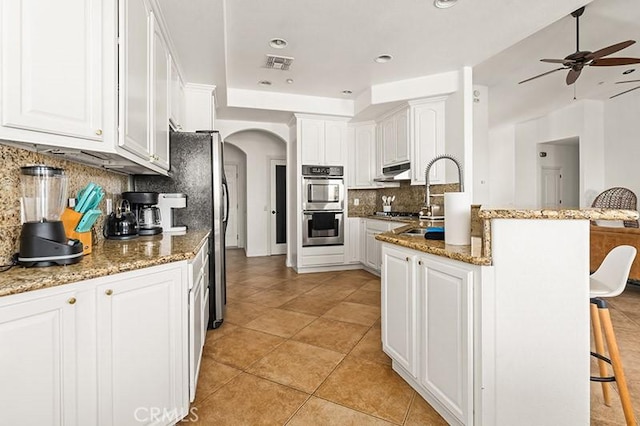 kitchen featuring a kitchen bar, white cabinets, tasteful backsplash, and stainless steel double oven