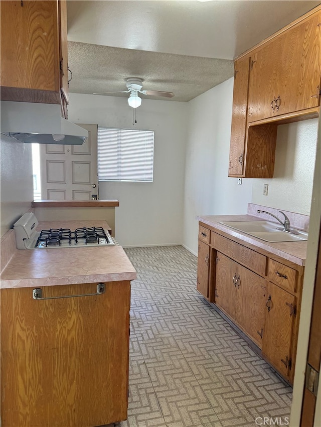 kitchen with ceiling fan, sink, gas cooktop, ventilation hood, and a textured ceiling