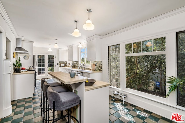 kitchen with hanging light fixtures, tasteful backsplash, wall chimney range hood, white cabinetry, and dark tile floors