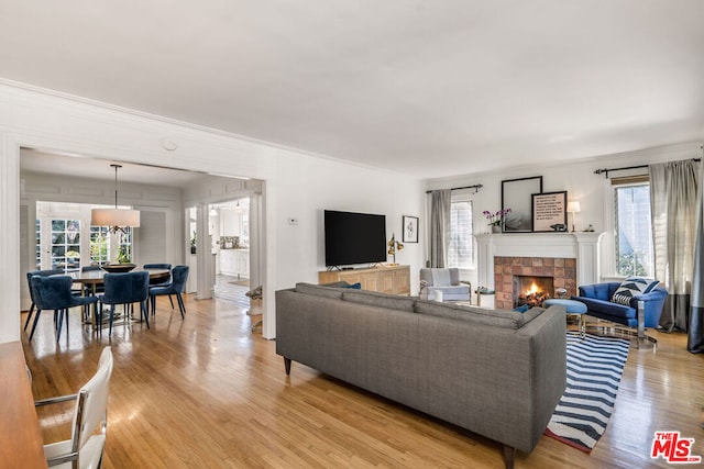 living room with a healthy amount of sunlight, light hardwood / wood-style flooring, a tile fireplace, and crown molding