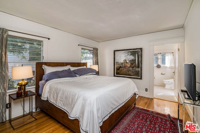 bedroom with ensuite bathroom, hardwood / wood-style floors, and multiple windows