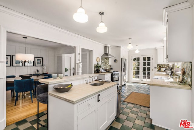 kitchen featuring wall chimney exhaust hood, sink, white cabinetry, a kitchen breakfast bar, and pendant lighting