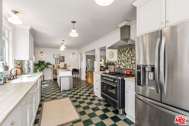 kitchen featuring dark tile flooring, wall chimney range hood, backsplash, range with gas stovetop, and stainless steel fridge with ice dispenser