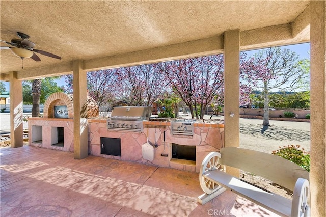 view of patio featuring ceiling fan, exterior kitchen, an outdoor fireplace, and grilling area