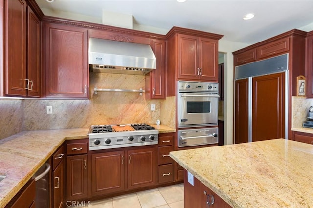 kitchen with appliances with stainless steel finishes, backsplash, light stone counters, wall chimney exhaust hood, and light tile patterned floors