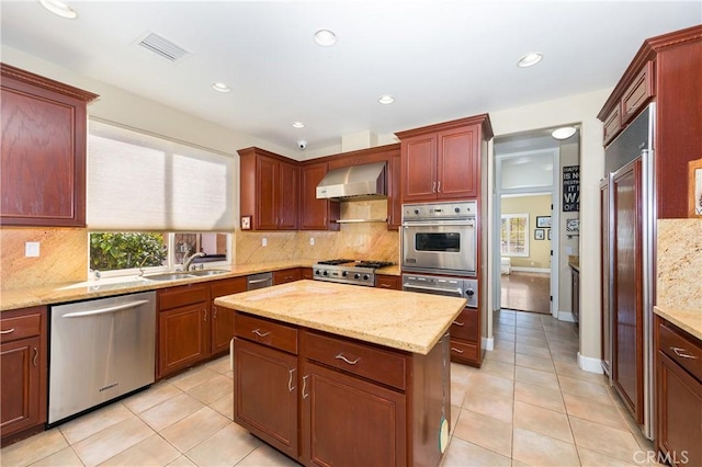 kitchen featuring sink, wall chimney range hood, light stone counters, light tile patterned floors, and appliances with stainless steel finishes