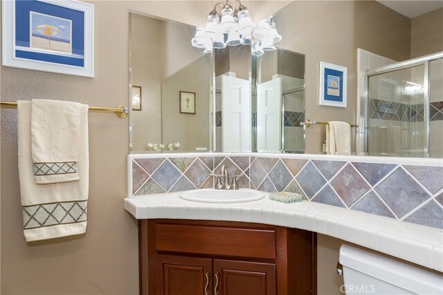 bathroom with backsplash, walk in shower, vanity, an inviting chandelier, and toilet