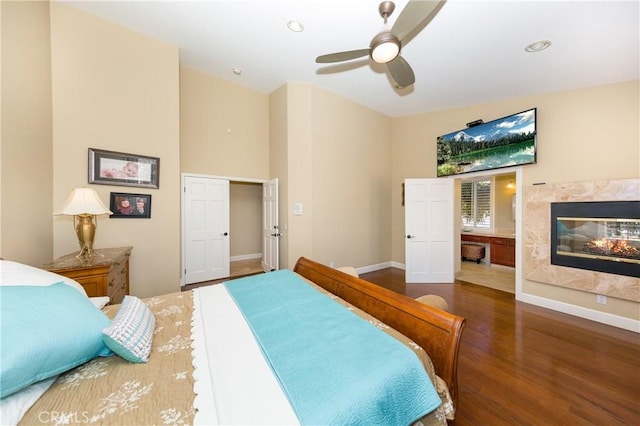 bedroom featuring a high end fireplace, dark hardwood / wood-style flooring, ceiling fan, and lofted ceiling