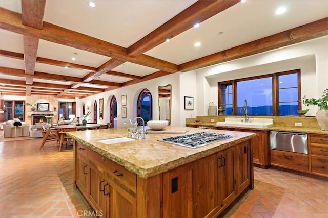 kitchen with beamed ceiling, stainless steel gas stovetop, sink, and a large island with sink