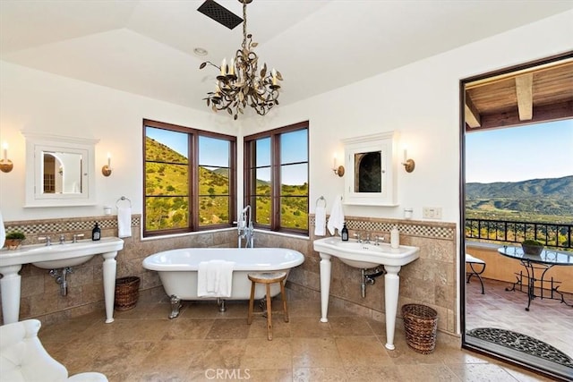 bathroom featuring a washtub, a mountain view, a chandelier, lofted ceiling, and tile walls