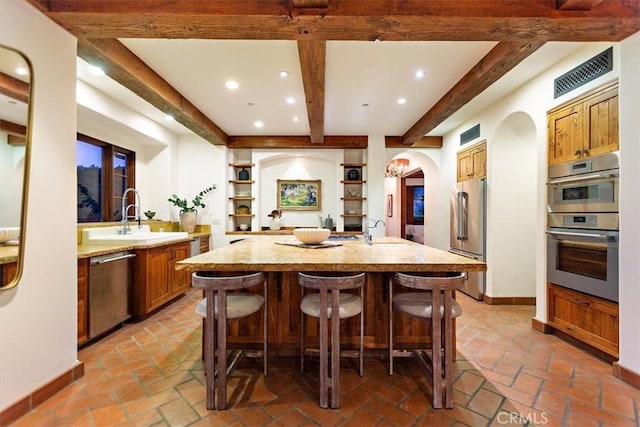 kitchen featuring appliances with stainless steel finishes, a breakfast bar, sink, beam ceiling, and a center island with sink