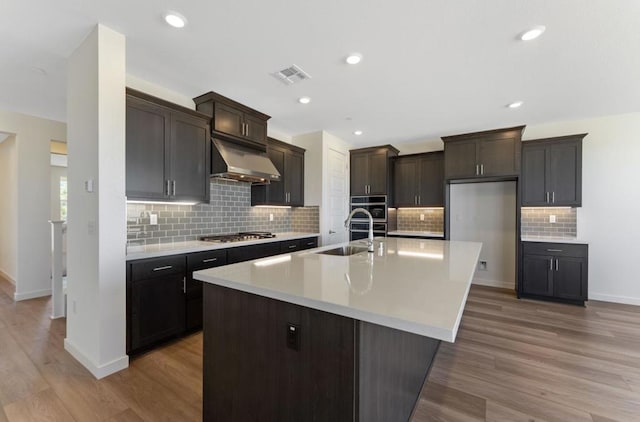 kitchen with exhaust hood, a center island with sink, light wood-type flooring, and sink