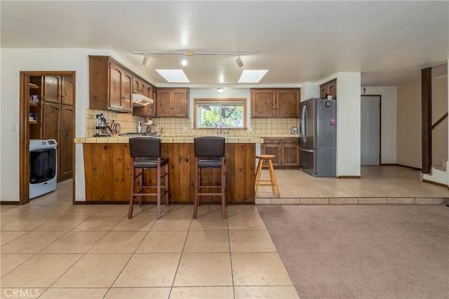 kitchen featuring a kitchen bar, track lighting, stainless steel refrigerator, washer / clothes dryer, and light tile patterned flooring