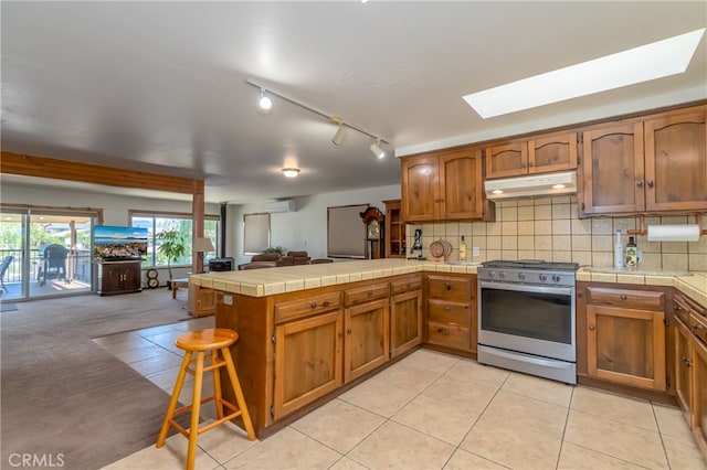 kitchen featuring tasteful backsplash, stainless steel range with gas cooktop, a skylight, light carpet, and kitchen peninsula