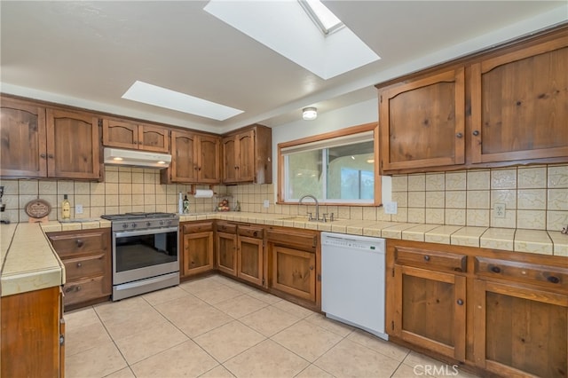 kitchen featuring gas range, light tile patterned flooring, decorative backsplash, a skylight, and white dishwasher