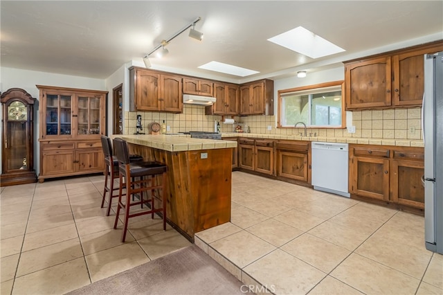 kitchen with decorative backsplash, a skylight, dishwasher, tile countertops, and light tile patterned floors