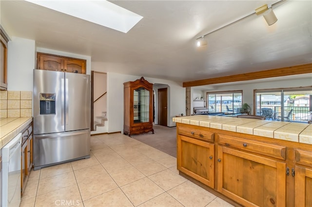 kitchen featuring a skylight, white dishwasher, light tile patterned floors, and stainless steel refrigerator with ice dispenser