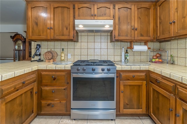 kitchen with decorative backsplash, stainless steel gas range oven, and light tile patterned floors