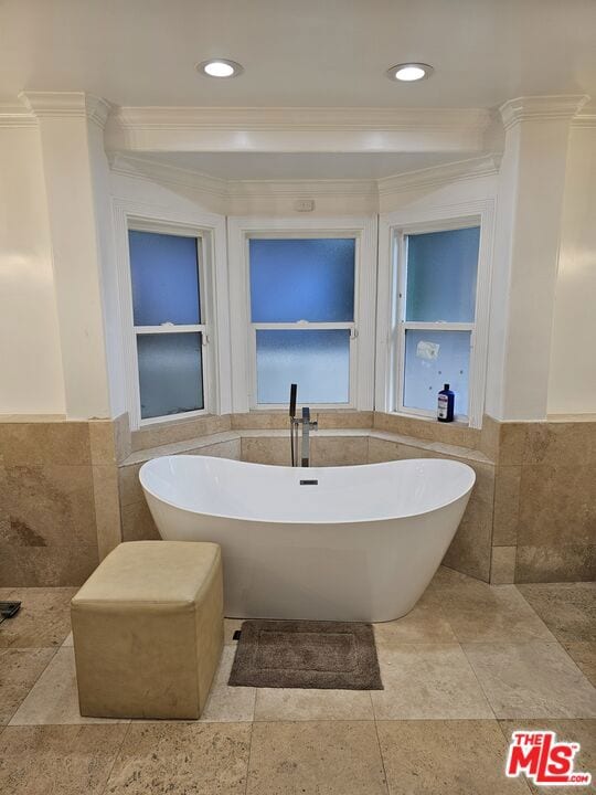 bathroom featuring crown molding, a washtub, and tile walls