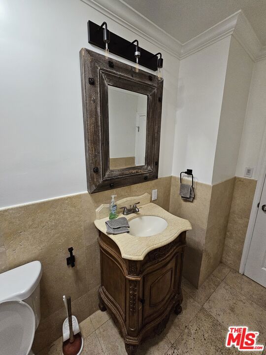 bathroom with vanity, toilet, ornamental molding, and tile walls