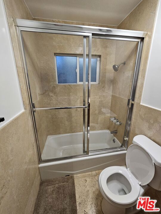 bathroom with toilet and shower / bath combination with glass door