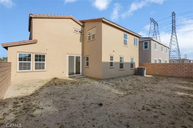 rear view of house with central air condition unit, stucco siding, a tiled roof, and fence