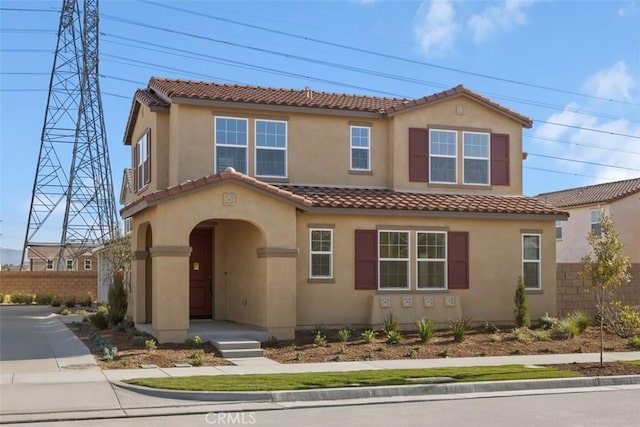 mediterranean / spanish-style home with a tiled roof, fence, and stucco siding