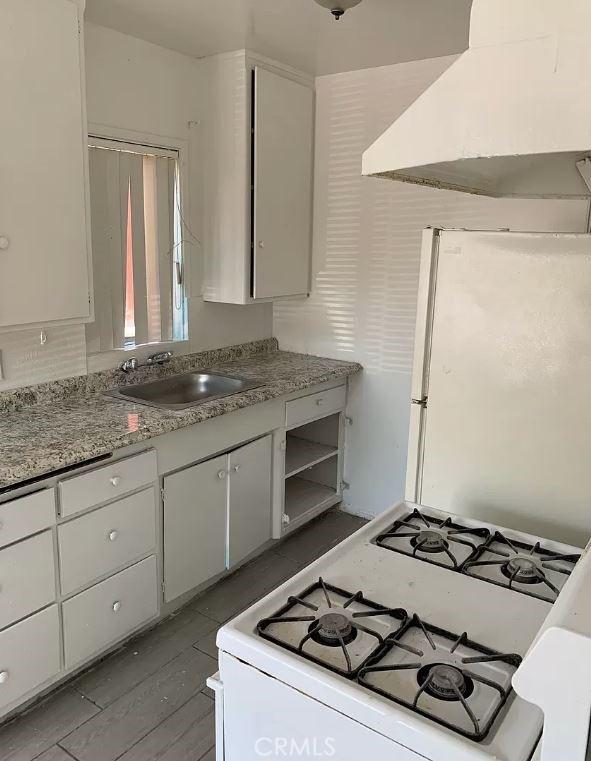 kitchen featuring white appliances, dark wood-type flooring, sink, range hood, and white cabinetry