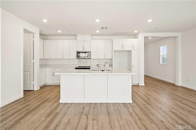 kitchen with white cabinetry, a center island with sink, sink, and light hardwood / wood-style flooring