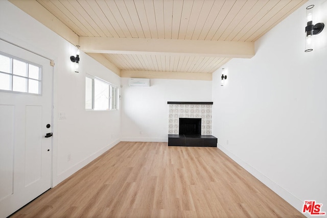 unfurnished living room featuring a fireplace, beam ceiling, an AC wall unit, and light wood-type flooring