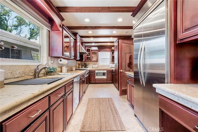 kitchen featuring built in appliances, decorative backsplash, sink, light stone counters, and beam ceiling