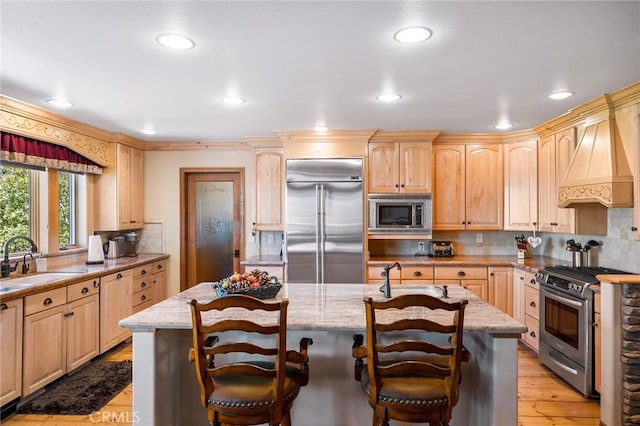 kitchen featuring built in appliances, light brown cabinets, a center island with sink, and sink