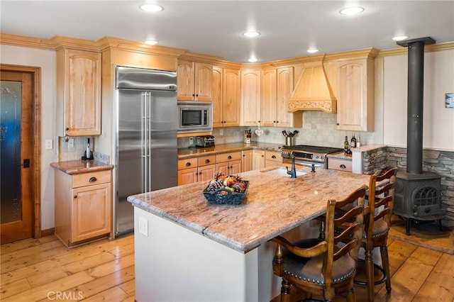 kitchen featuring light brown cabinets, a wood stove, built in appliances, light hardwood / wood-style floors, and light stone counters